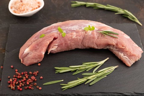 Raw pork meat with herbs and spices on slate cutting board on black concrete background. Side view,