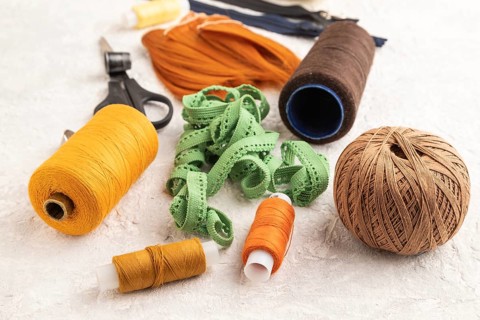 Sewing accessories: scissors, thread, thimbles, braid on gray concrete background. Side view, close