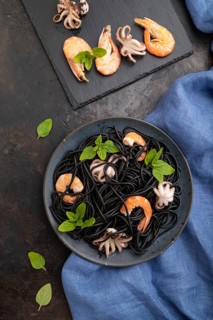 Black cuttlefish ink pasta with shrimps or prawns and small octopuses on black concrete background
