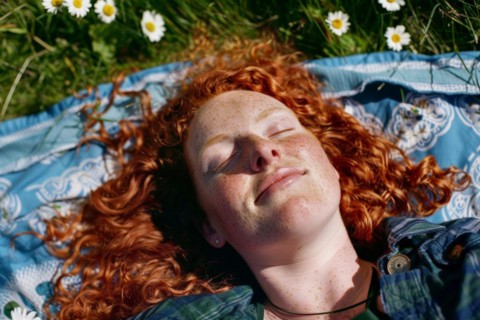 Teenager, young fair-skinned woman with red hair and freckles lying on a spring meadow and basking