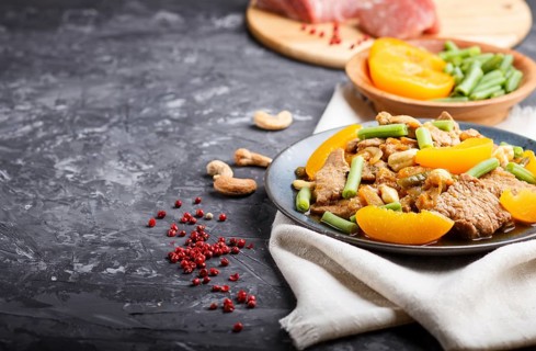 Fried pork with peaches, cashew and green beans on a black concrete background. side view, copy