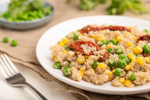Quinoa porridge with green pea, corn and dried tomatoes on ceramic plate on a white wooden