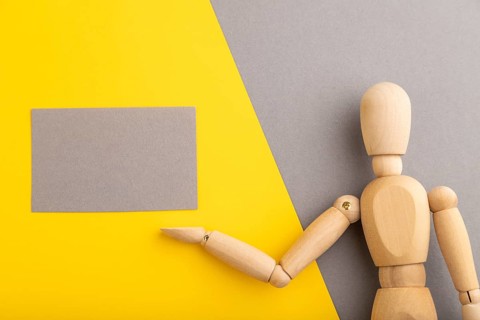 Wooden mannequin holding gray blank poster on gray and yellow pastel background. copy space,