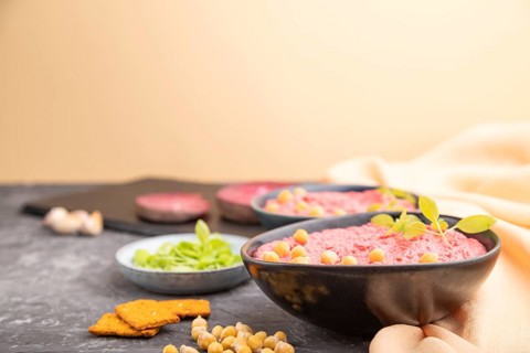 Hummus with beet and microgreen basil sprouts in ceramic bowl on a black concrete background and