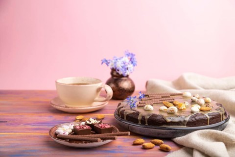 Homemade chocolate brownie cake with caramel cream and almonds with cup of coffee on a colored and