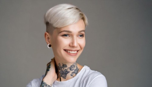 Portrait of a cheerful woman with a short haircut and visible tattoos in front of a grey