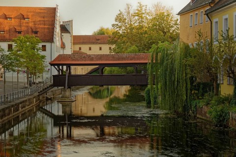 The old ship bridge leads over the calm river Vils with reflection in the water, Amberg, Upper