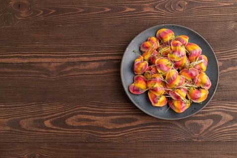 Rainbow colored dumplings with pepper, herbs, microgreen on brown wooden background. Top view, flat