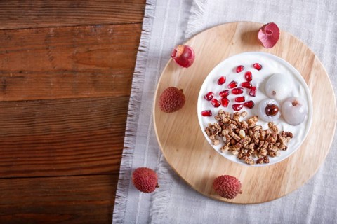 Greek yogurt with lychee, pomegranate seeds and granola in a white plate on a brown wooden