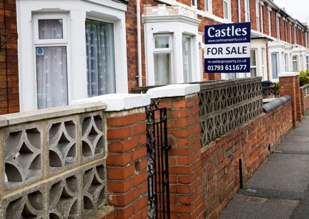 Estate agent for sale sign outside red brick terraced house in central Swindon, England, United
