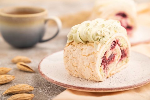 Roll biscuit cake with cream cheese and jam, cup of coffee on brown concrete background and orange