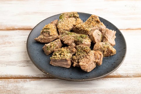 Stewed turkey fillet with garlic on white wooden background. Side view, close up