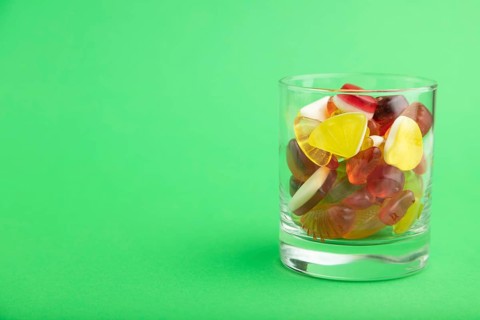 Various fruit jelly candies in drinking glass on green pastel background. side view, copy space