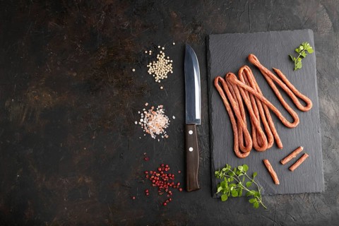 Traditional polish smoked pork sausage kabanos on a slate cutting board with salt and pepper on