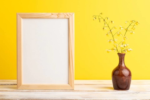 Wooden frame with yellow barrenwort flowers in ceramic vase on yellow pastel background. side view,