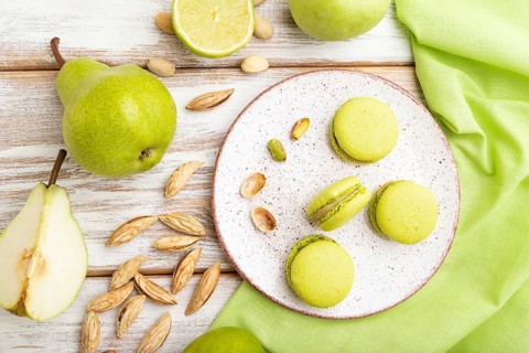 Green macarons or macaroons cakes with cup of coffee on a white wooden background and green linen