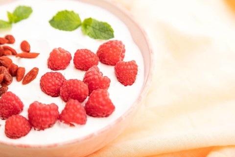 Yogurt with raspberry and goji berries in ceramic bowl on white concrete background and orange