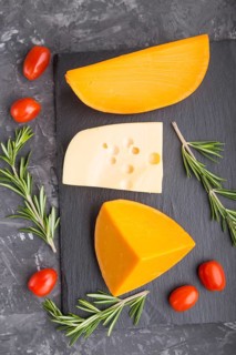 Various types of cheese with rosemary and tomatoes on black slate board on a black concrete