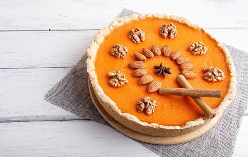 Traditional american sweet pumpkin pie decorated with nuts, on white wooden background. close up
