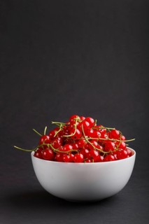Fresh red currant in white bowl on black background. side view, copy space