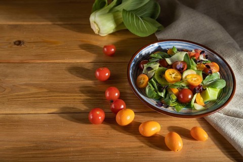 Vegetarian salad of pac choi cabbage, kiwi, tomatoes, kumquat, microgreen sprouts on a wooden