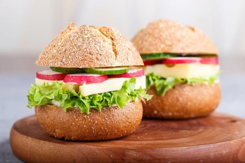 Sandwiches with cheese, radish, lettuce and cucumber on wooden board on a gray concrete background.