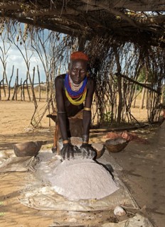 Woman from the Arbore ethnic group grinding red sorghum millet on a grinding stone, Southern Omo