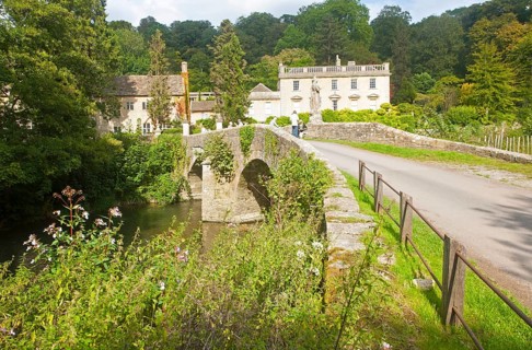 Bridge crossing the River Frome and the classical Georgian facade of Iford Manor, near Freshford,