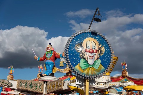 Colourfully decorated carousel with clown figure and blue sky in the background at a fairground,