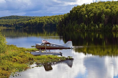 Seaplane Beaver de Havilland stands on the shore of a crystal-clear lake and is reflected in the