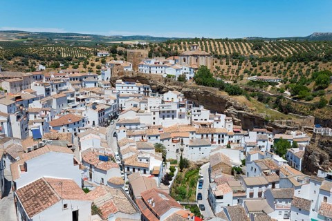 A white village with tiled roofs, embedded in a rock formation, surrounded by rural landscape, cave