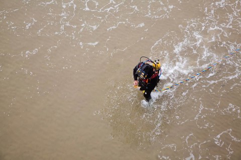 Looking down from above at professional diver on a beach about to enter the sea to work on the pier