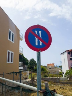 Red traffic sign with blue and white no parking symbol in front of buildings and a clear sky, no