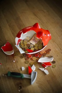 Symbolic photo on the subject of saving. An open, broken piggy bank with coins and banknotes stands