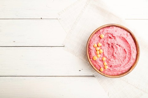 Hummus with beet in wooden bowl on a white wooden background and linen textile. Top view, flat lay,