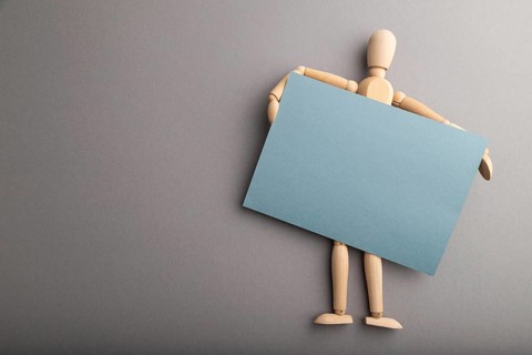 Wooden mannequin holding blue blank poster on gray pastel background. copy space, isolated,