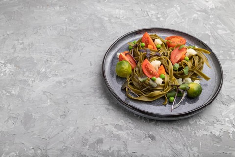 Tagliatelle green spinach pasta with tomato, pea and microgreen sprouts on a gray concrete