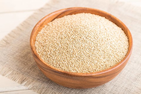 Wooden bowl with raw white quinoa seeds on a white wooden background and linen textile. Side view,