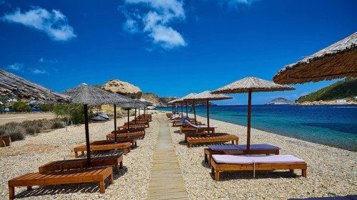 A beach with a wooden walkway and deckchairs under thatched umbrellas, the view of the clear water