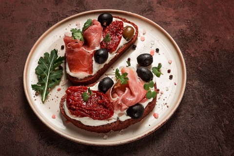 Sandwiches with cheese and prosciutto, dried tomatoes and olives, breakfast on a plate