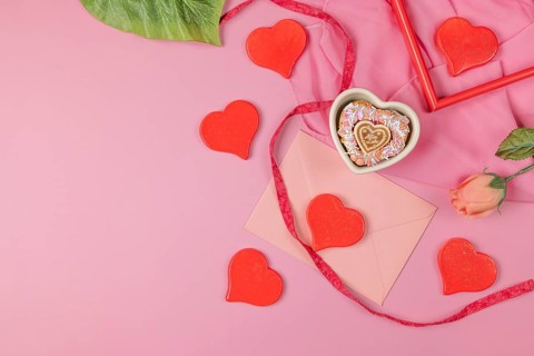 Bright red hearts scattered around a pink envelope and a single rose, Valentine's Day, heart-shaped