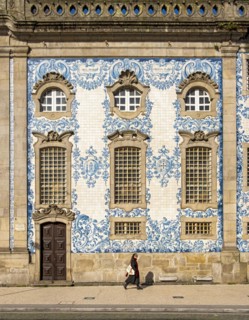 Woman passes by the facade of Igreja do Carmo church, adorned with intricate blue and white tiles,