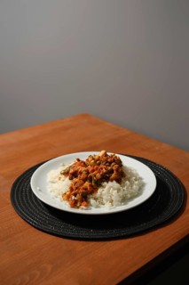 Homemade chicken stew with corn, peas, tomato, bell pepper and rice on wooden kitchen table