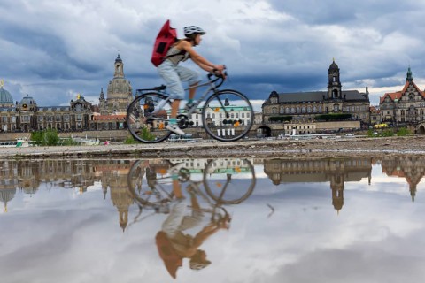 The Dresden silhouette with a cyclist and dark clouds behind the Church of Our Lady is reflected in