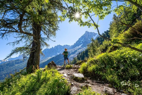 Hiker on hiking trail with sun star, hiking trail La Jonction, behind summit of Aiguille du Midi,