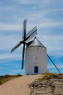 An old windmill under a blue sky with clouds at the end of a dirt road in a rural landscape,