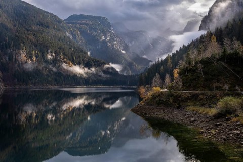 The Vordere Gosausee in autumn. In the background, the Dachstein mountain range in clouds. Cloudy