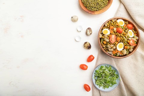 Mung bean porridge with quail eggs, tomatoes and microgreen sprouts on a white wooden background
