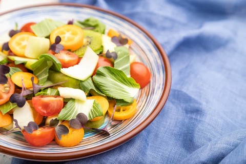 Vegetarian salad of pac choi cabbage, kiwi, tomatoes, kumquat, microgreen sprouts on a white