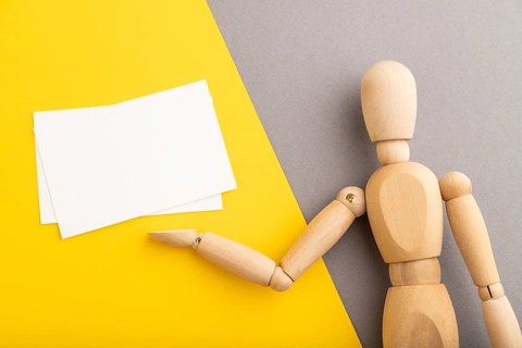 Wooden mannequin holding white blank poster on gray and yellow pastel background. copy space,